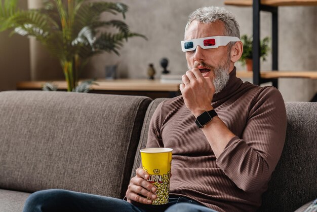 Älterer Mann, der zu Hause 3D-Filme mit Popcorn anschaut