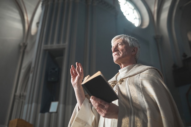 Älterer Mann im Kostüm, der die Bibel liest, während er in der Kirche dient