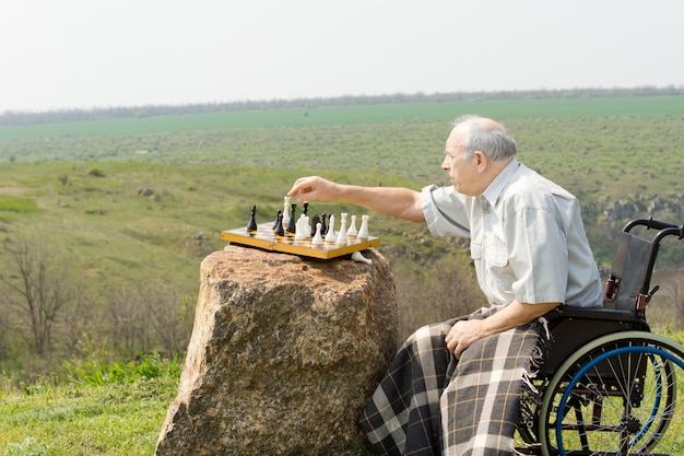 Älterer Mann in einem Rollstuhl, der draußen Schach spielt