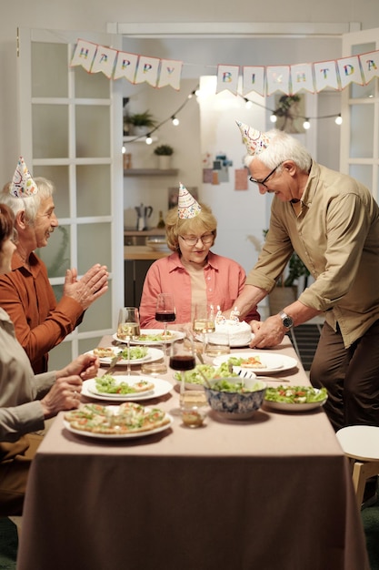 Älterer Mann klatscht in die Hände, während er der alten Frau zu ihrem Geburtstag gratuliert