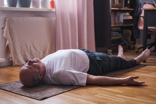 Älterer Mann meditiert auf einem Holzboden und liegt in Shavasana-Pose.