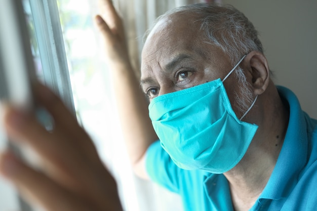 Älterer Mann mit Gesichtsmaske, die durch Fenster schaut