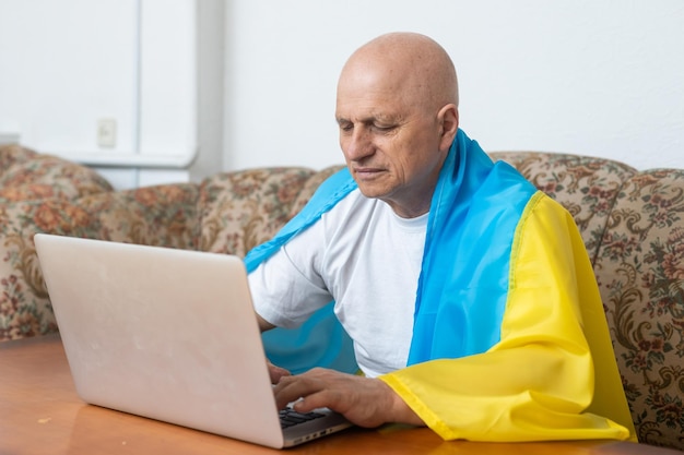 Älterer Mann mit Laptop und Ukraine-Flagge