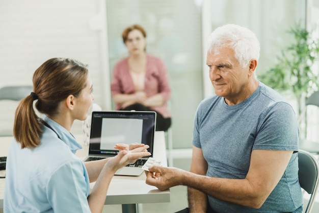 Älterer Mann spricht und berät sich mit einer jungen Ärztin über seine Medizintherapie in einer modernen Klinik.