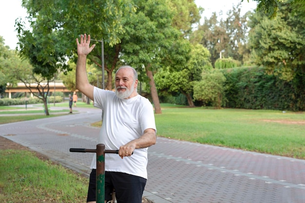 Älterer Mann trainiert im Fitnessstudio im Freien im Park und winkt