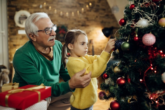 Älterer Mann und seine Enkelin schmücken den Weihnachtsbaum zu Hause