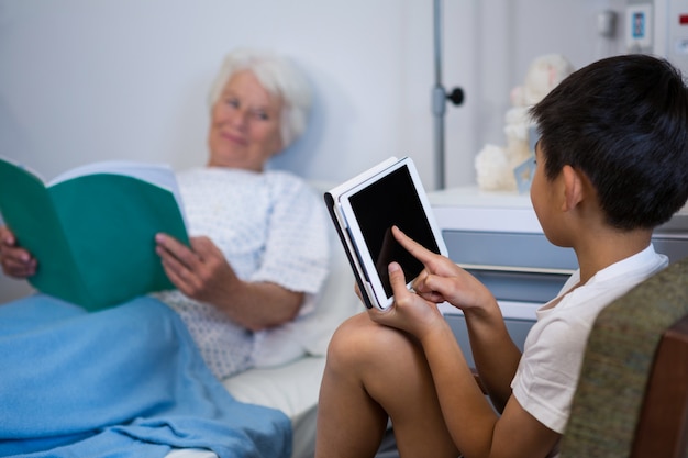 Älterer Patient, der ein Buch liest, während Junge digitales Tablett verwendet