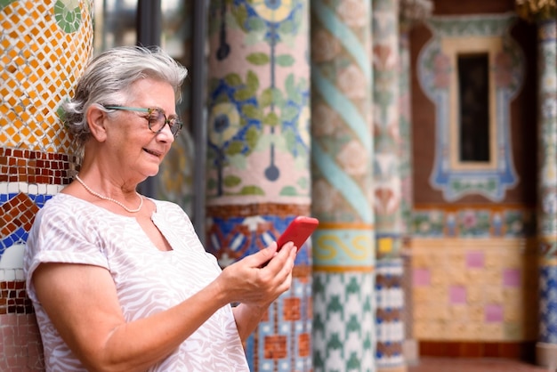 Älterer Reisender in der europäischen Stadt, der draußen vor der Musikhalle in Barcelona steht Ältere attraktive grauhaarige Dame mit Handy in der Nähe von Mosaiksäulen