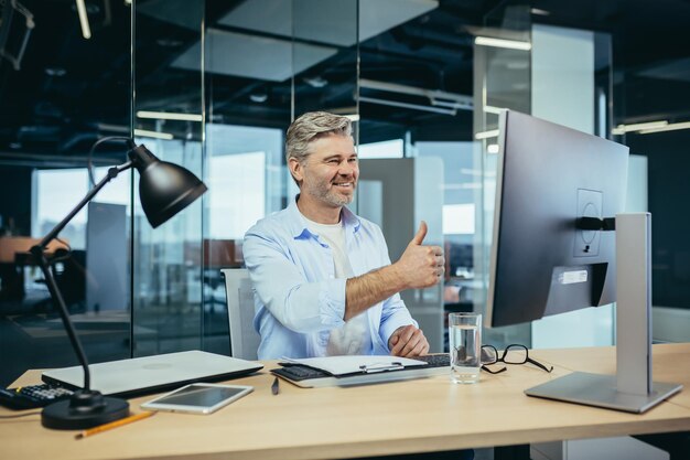 Älterer und erfahrener Mitarbeiter berät den Käufer bei einem Videoanruf. Der Mann arbeitet in einem modernen Büro und verwendet eine Webcam