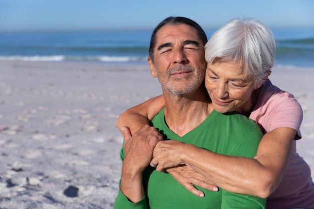 Älteres kaukasisches Paar genießt die Zeit am Strand, eine Frau umarmt einen Mann von hinten