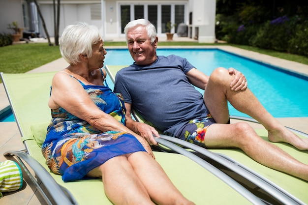 Älteres Paar, das auf dem Liegestuhl am Pool miteinander interagiert