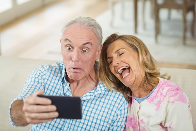 Älteres Paar, das ein Selfie auf Handy im Wohnzimmer nimmt