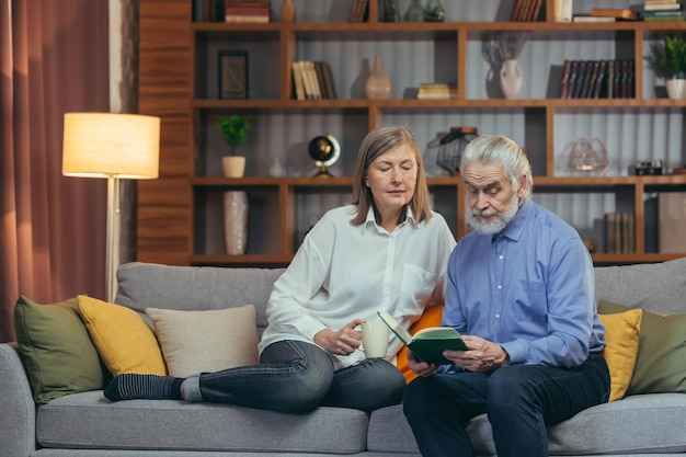 Älteres Paar, das Freizeit damit verbringt, ein Buch zu lesen, das zusammen auf einem gemütlichen Sofa zu Hause sitzt