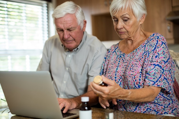 Älteres Paar, das Laptop und Pillenflasche in der Küche zu Hause hält
