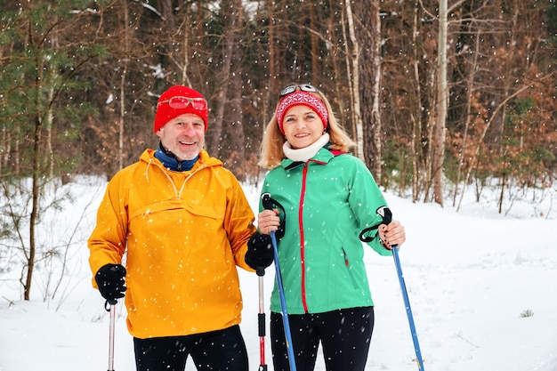 Älteres Paar, das mit nordischen Wanderstöcken im verschneiten Winterpark geht