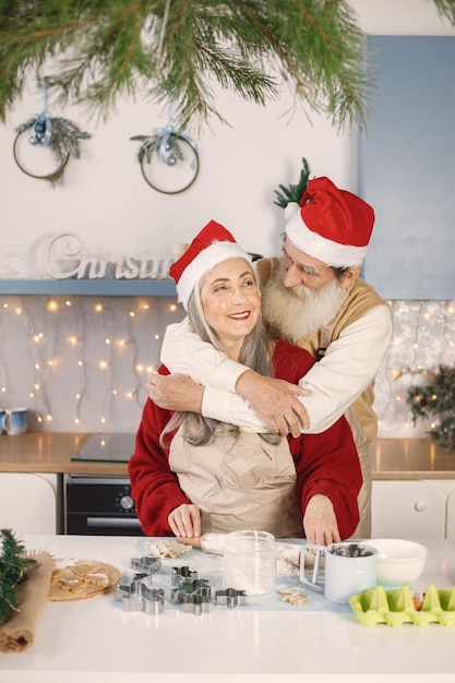 Älteres Paar in Schürzen und weihnachtlichen roten Hüten, die Kekse in der Küche backen