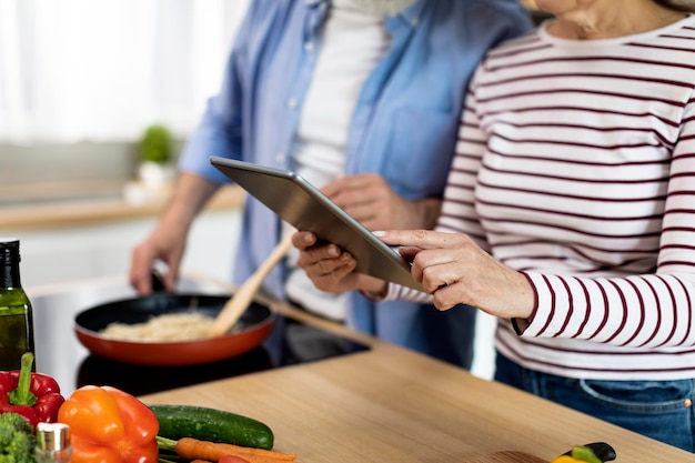 Älteres Paar mit digitalem Tablet in der Küche beim Kochen von Speisen