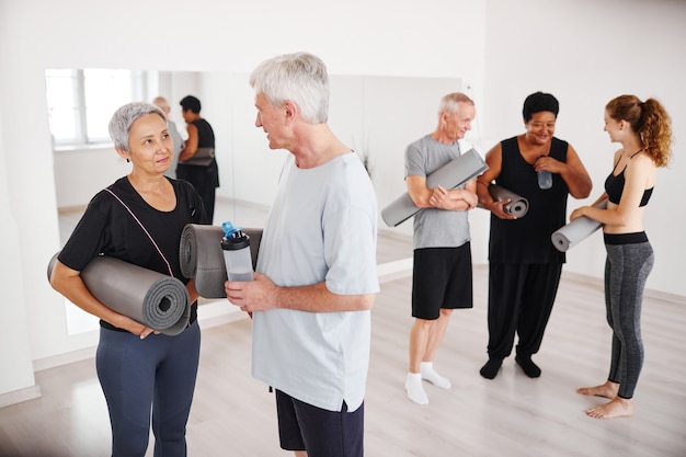 Älteres Paar mit Gymnastikmatten, die nach dem Yoga-Kurs mit anderen Leuten im Hintern miteinander sprechen.