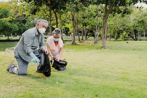 Älteres Paar mit Masken sammelt freiwillig recycelte Plastikflaschen in schwarzen Säcken