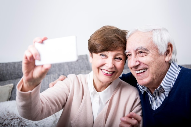 Älteres Paar sitzt auf der Couch und macht ein Smartphone-Selfie