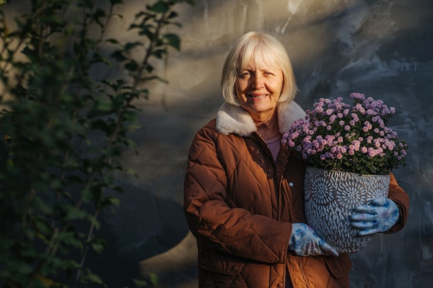 Älteres Weibchen mit Blumen an einem sonnigen Frühlingstag. Ältere Frau in Oberbekleidung mit Topfblumen