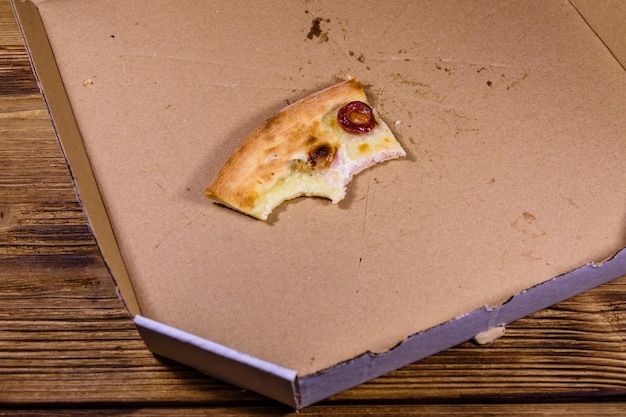 Última porción de pizza con salchichas, jamón y queso parmesano en una caja de cartón