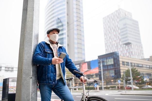 Último homem com bicicleta e smartphone em pé ao ar livre na rua na cidade, o conceito de coronavírus.