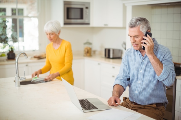 Último homem falando no celular enquanto mulher lavando o prato na cozinha