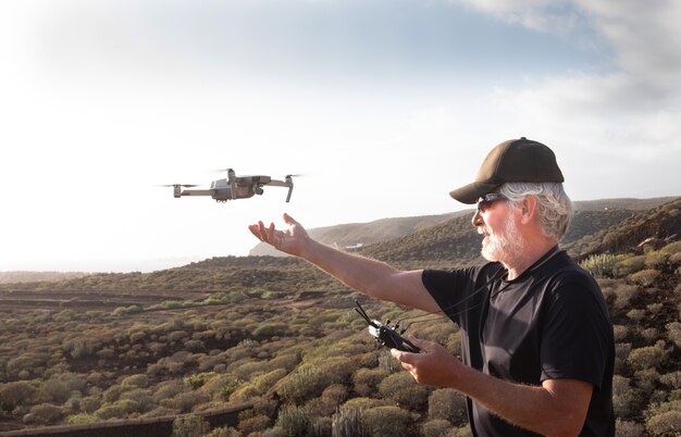 Último homem se divertir com o drone na cordilheira. Olhando para o vôo sob o pôr do sol. Um povo caucasiano casual com barba e cabelos brancos