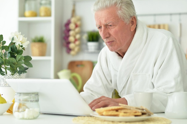 Último homem sentado à mesa na cozinha usando um laptop moderno