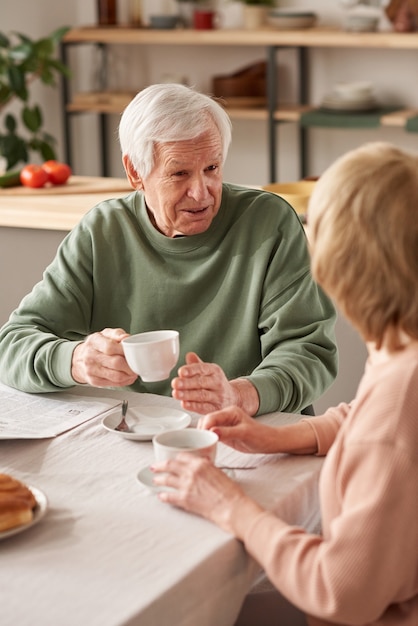 Último homem sentado à mesa tomando chá com sua esposa e conversando na cozinha