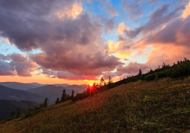 Últimos raios de sol no céu noturno com nuvens. Vista para a montanha do pôr do sol de verão (Cárpatos, Ucrânia).