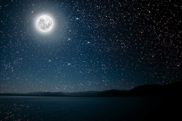 Lua contra um céu estrelado de noite brilhante refletido no mar.