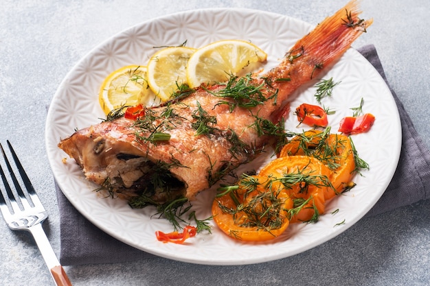 Lubina al horno con tomate pimiento limón y hierbas en plato de cerámica.