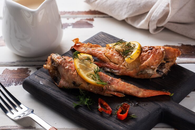 Lubina al horno con tomate pimiento limón y hierbas sobre soporte de pizarra negra