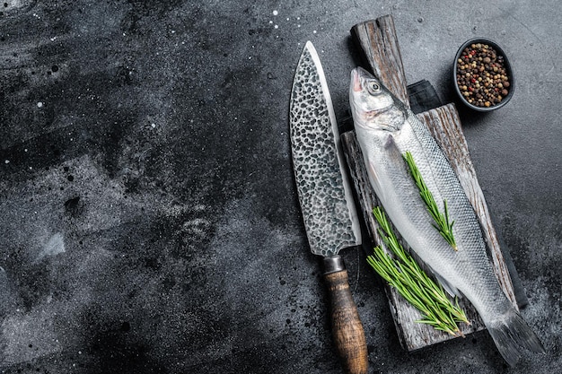 Lubina cruda fresca o pescado de lubina sobre una tabla de madera lista para cocinar. Fondo negro. Vista superior. Copie el espacio.