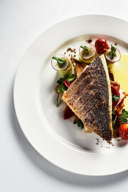 Lubina a la plancha con tomate frito, acompañada de patatas. Vista superior del plato de pescado, fondo claro, espacio de copia.