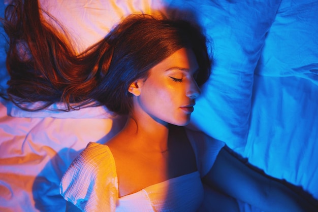 Luces de la bella durmiente y mujer con sueño e iluminación de neón creativa Descansando la cara y el modelo brillan y se sienten relajados y tranquilos en una almohada de cama con perfil estético en una cama de dormitorio en casa