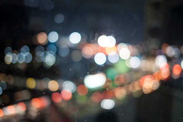 Las luces de bokeh en la lluvia miran por la ventana.