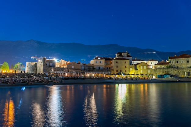 Las luces de la ciudad nocturna se reflejan en las aguas costeras.