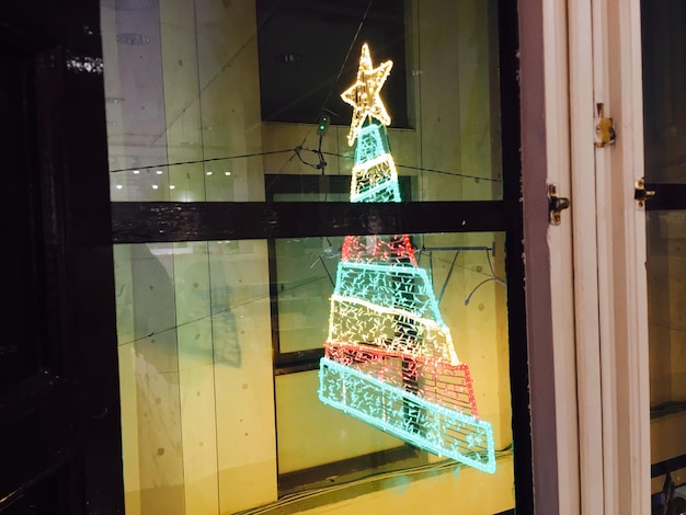 Foto luces navideñas iluminadas colgando del edificio vistas a través de una ventana de vidrio por la noche