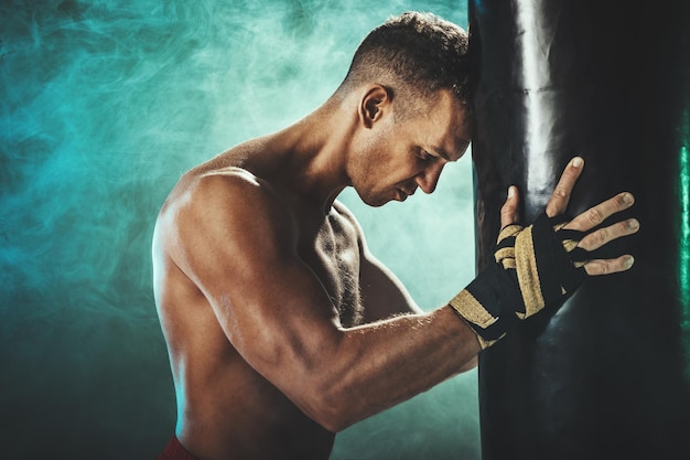 Un luchador cansado descansa después de un fuerte entrenamiento de boxeo con saco de boxeo.