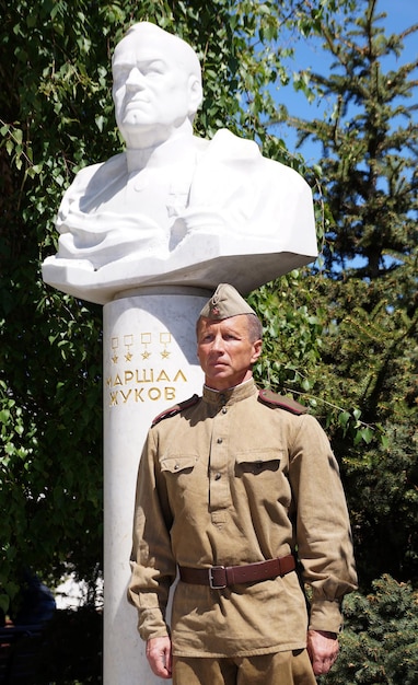 Luchador del Ejército Rojo en forma de tiempos de la Segunda Guerra Mundial cerca de un busto del mariscal Zhukov con la inscripción "Mariscal Zhukov"