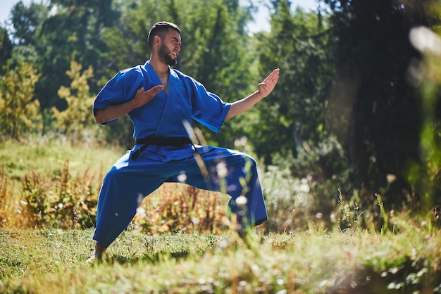 Luchador de karate kazajo asiático es combate en kimono azul uniforme en un hermoso paisaje de verano con espacio de copia