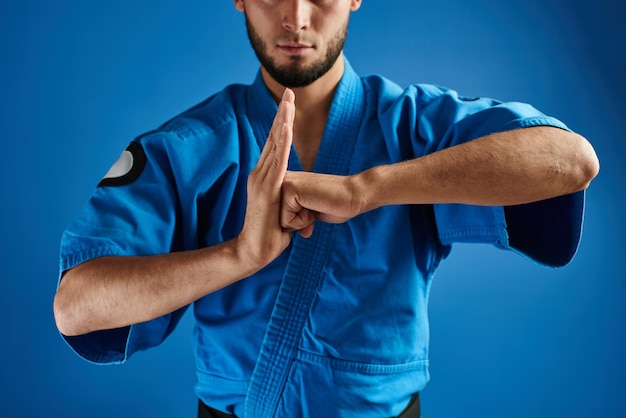 Luchador de karate kazajo asiático en uniforme de kimono que muestra el gesto de las manos sobre fondo azul aislado en estudio