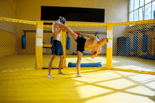 Luchador de MMA masculino hace patada alta a su oponente en una jaula en el gimnasio.