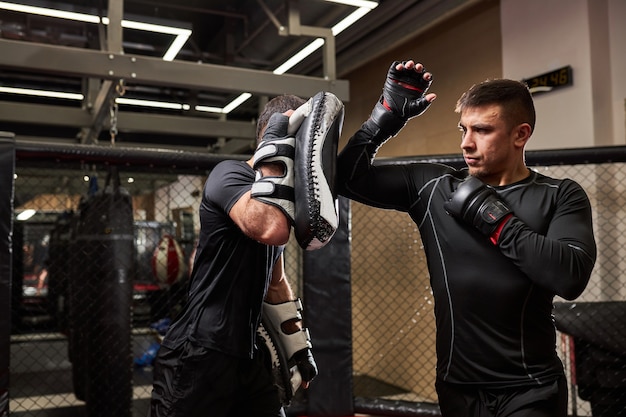 Luchador profesional de mma enseña trucos de autodefensa, mostrándoselos al joven boxeador. practicar diferentes técnicas juntos. deporte, concepto de entrenamiento. Espacio de copia de vista lateral