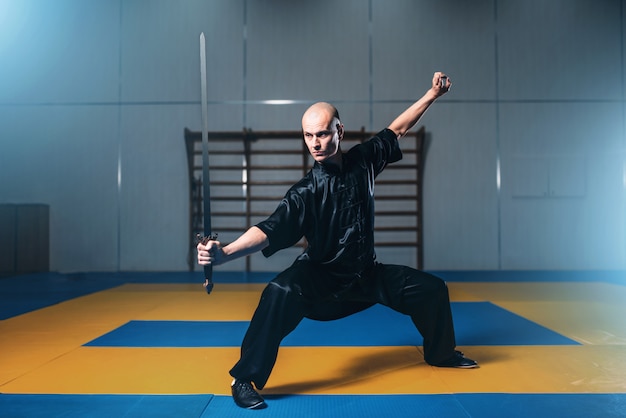 Luchador de Wushu con espada en acción, artes marciales. Hombre de paño negro posa con hoja