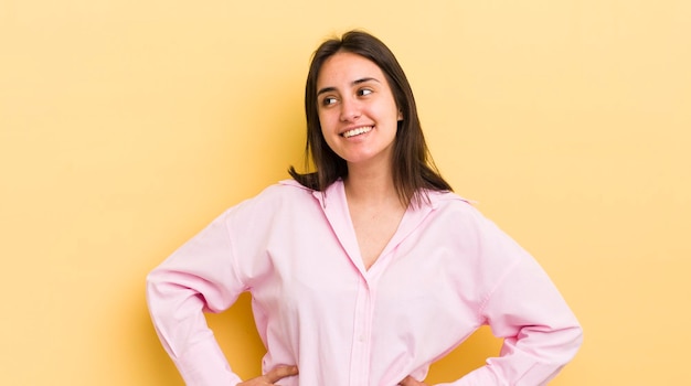 Luciendo feliz, alegre y confiado, sonriendo con orgullo y mirando hacia un lado con ambas manos en las caderas