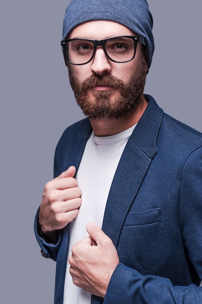 simplemente perfecto. hombre barbudo joven guapo en ropa de sport elegante mirando a la cámara mientras está de pie el fondo gris | Foto Premium